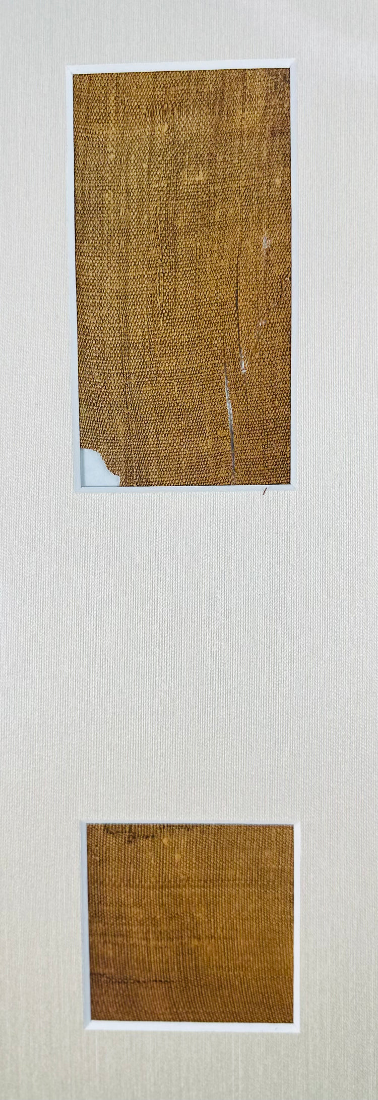 Two golden-brown woven linen fragments attributed to Manchester Mummy 1770, mounted vertically on a cream fabric background.