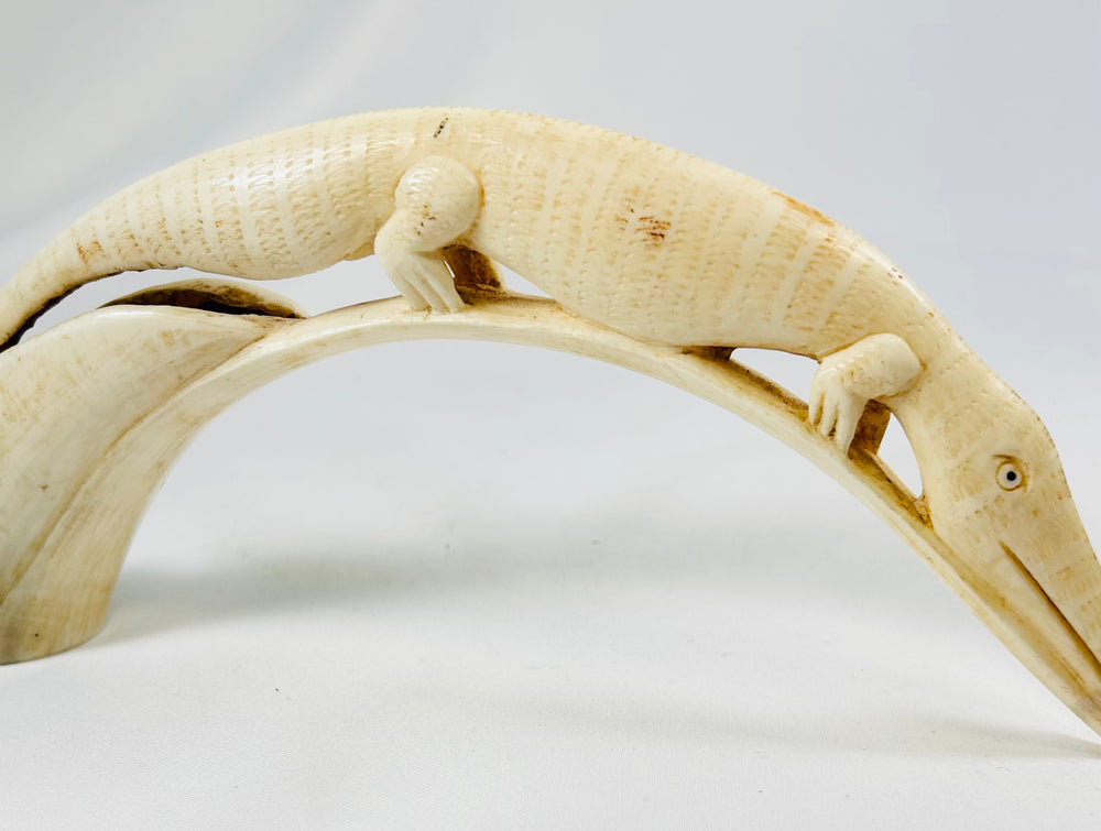Detailed view of an African hippopotamus tooth carving depicting a crocodile motif, handcrafted early 20th-century ivory artwork displayed on a white background.