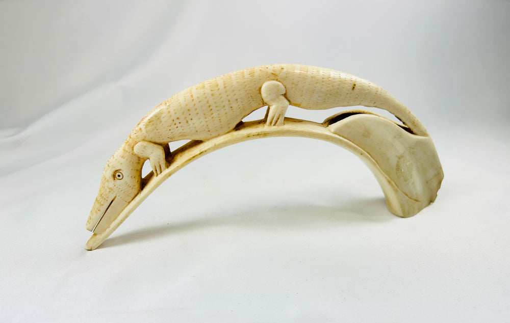 Angled view of a carved African hippopotamus tooth featuring a crocodile motif, early 20th-century tribal ivory artwork with intricate detail and natural patina on white background.