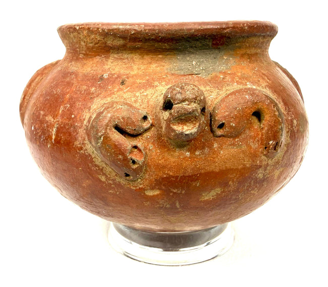 Ancient American terracotta ceramic vessel featuring a rounded profile, ornamental relief details, scattered surface abrasions, and darker areas of patination.