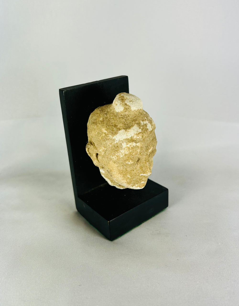 Three-quarter right view of a Gandharan Buddha head carved from stone, mounted on a black stand.