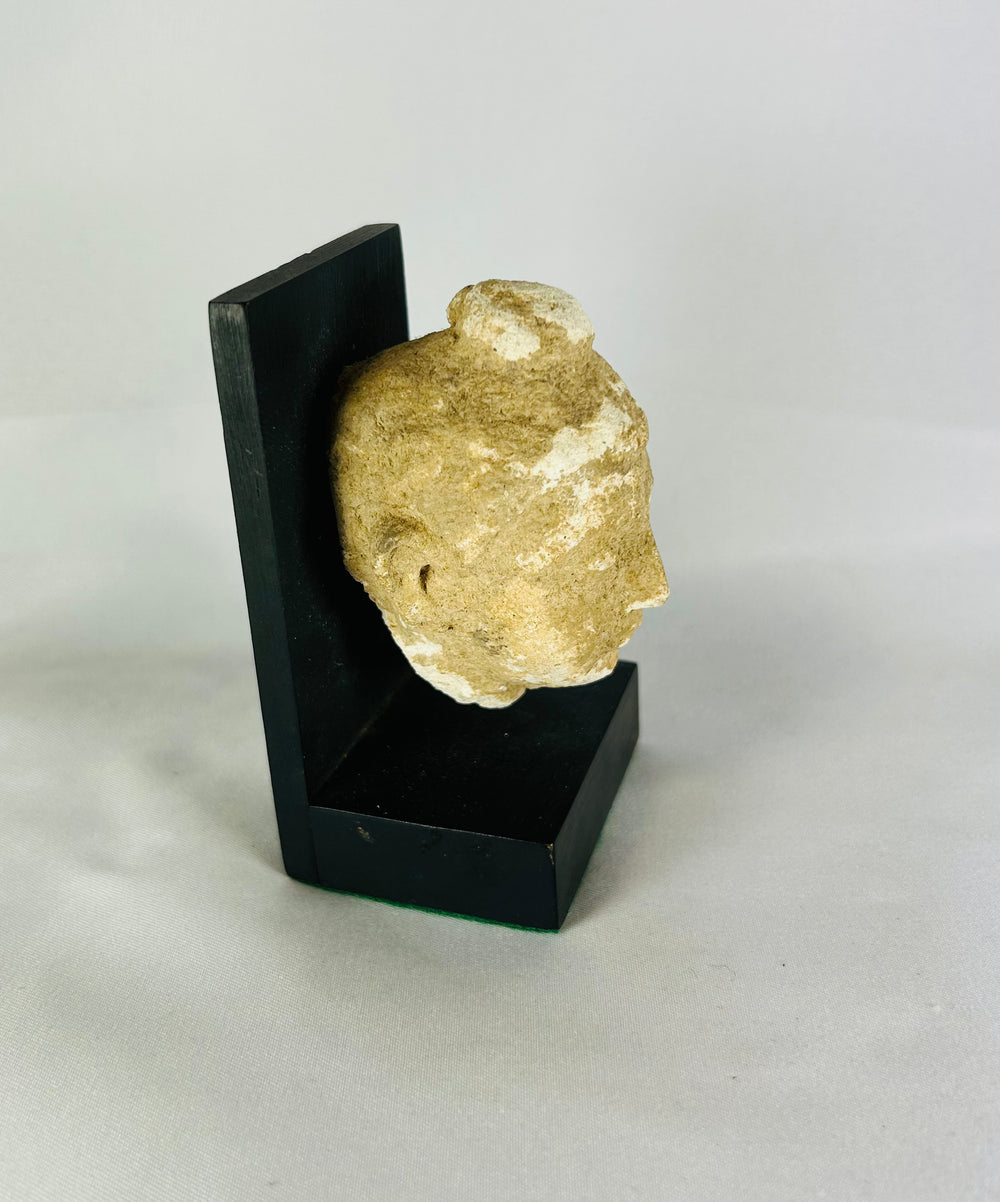 Profile view of the Gandharan stone Buddha head showing patina, mounted on a modern black display stand.