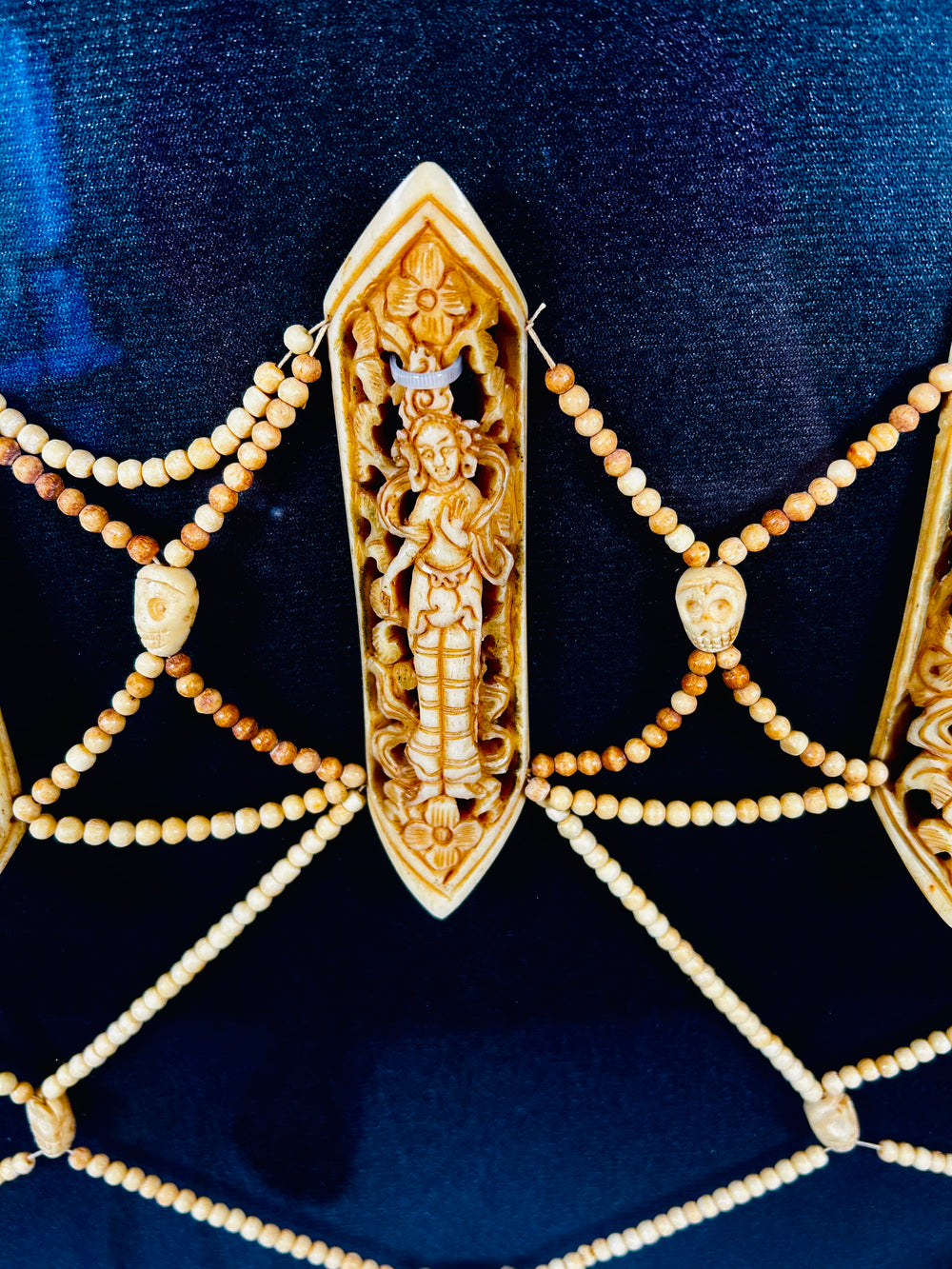 Close-up of 19th-century Tibetan Tantric ritual apron (rus gyan) plaque carved from human bone, depicting Chakrasamvara deity amid intricate beadwork on deep blue background