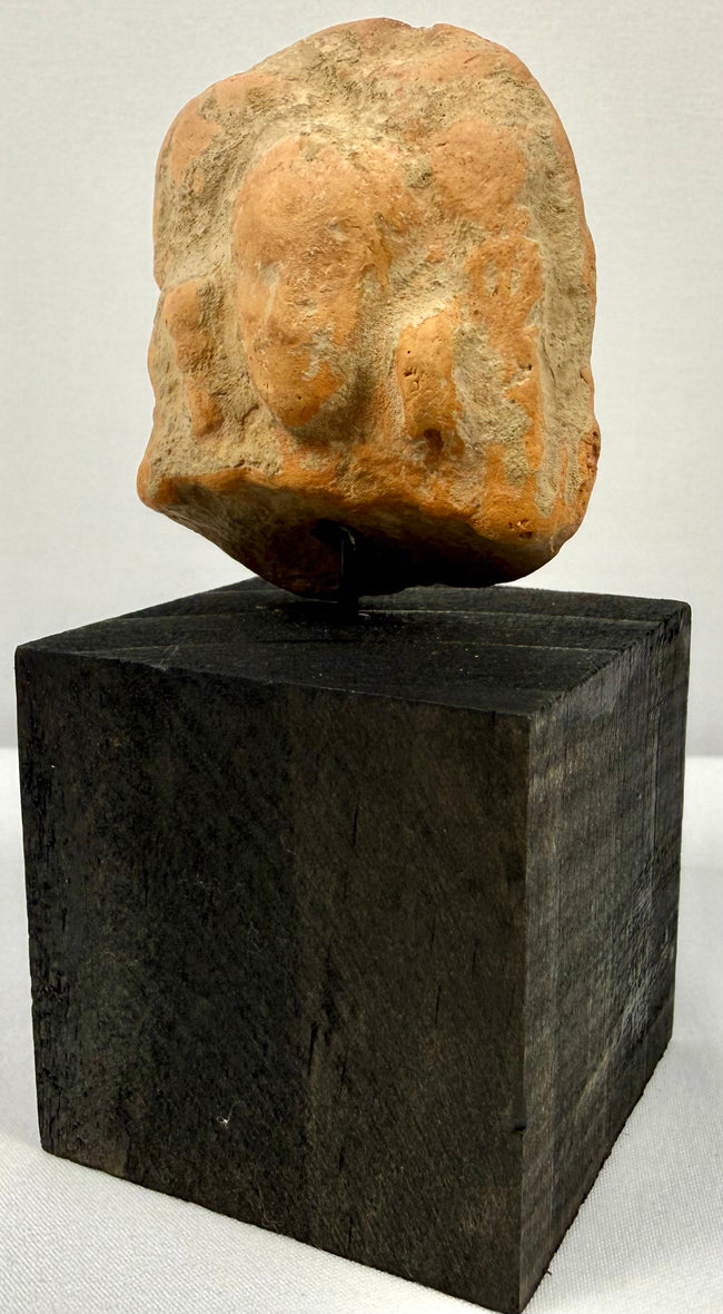 Frontal view of ancient orange-brown terracotta plaque with central bust and side figures