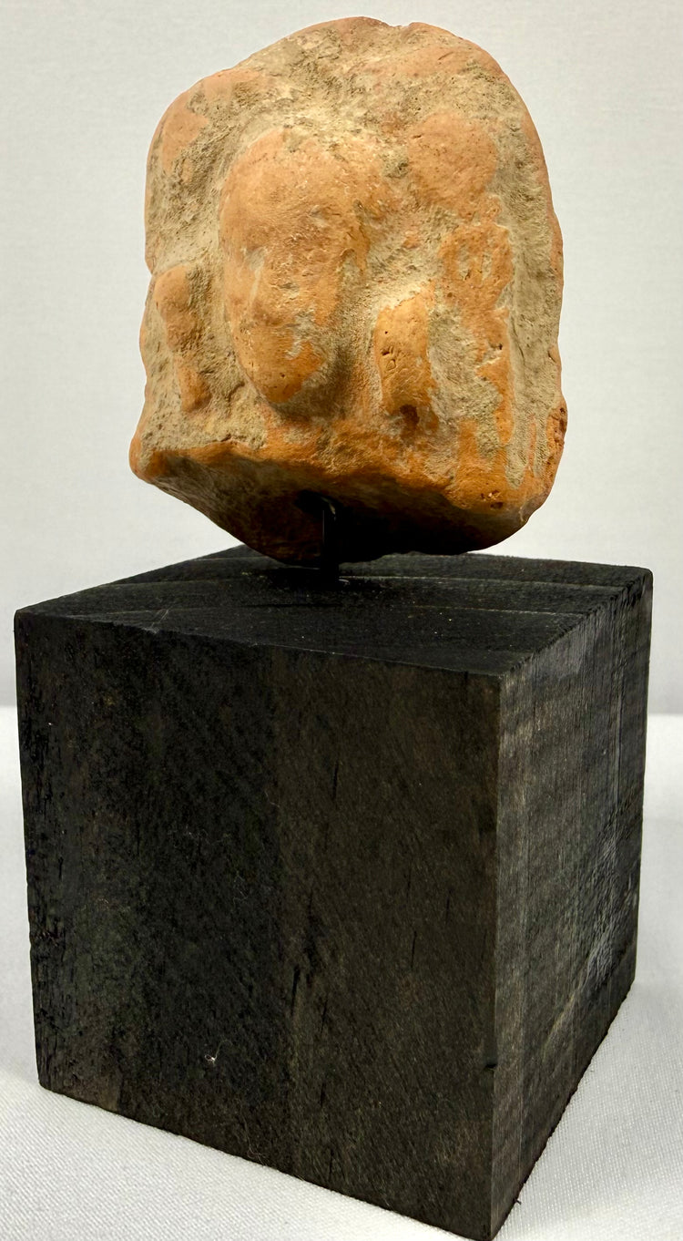 Frontal view of ancient orange-brown terracotta plaque with central bust and side figures