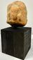 Frontal view of ancient orange-brown terracotta plaque with central bust and side figures