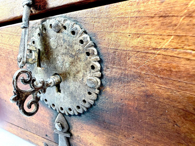 Macro shot of ornate dark iron key with scrolled bow inserted into perforated lock plate on elmwood box