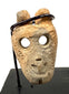 Frontal view of beige carved bone miniature anthropomorphic mask pendant with hollow eyes