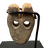 Stylized human face carving with symmetrical round eye holes and central nose bridge