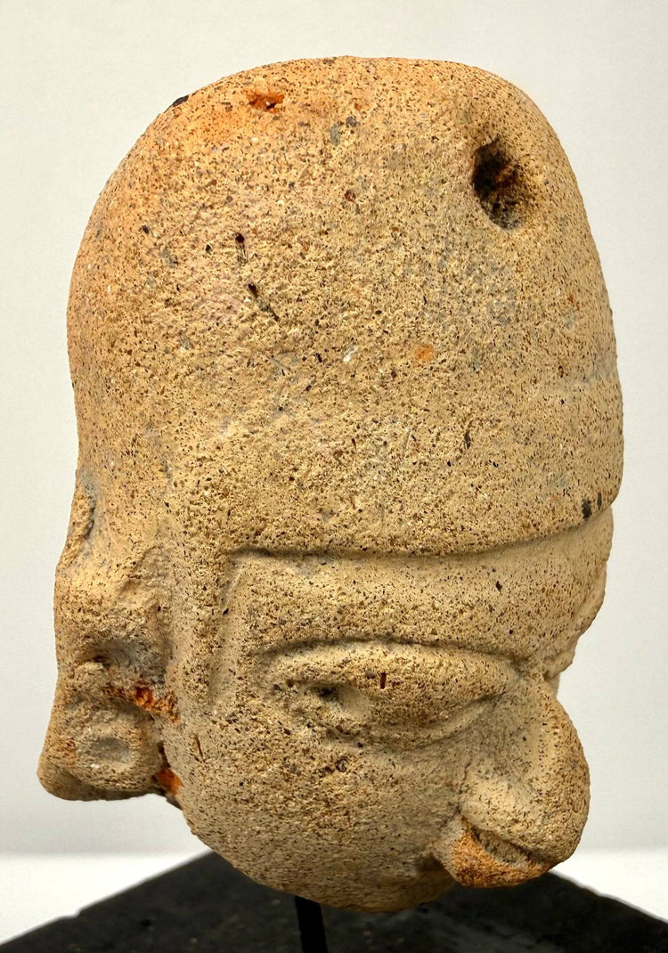 Three-quarter view of ancient clay pendant emphasizing eye sockets and headdress perforation