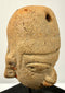 Three-quarter view of ancient clay pendant emphasizing eye sockets and headdress perforation