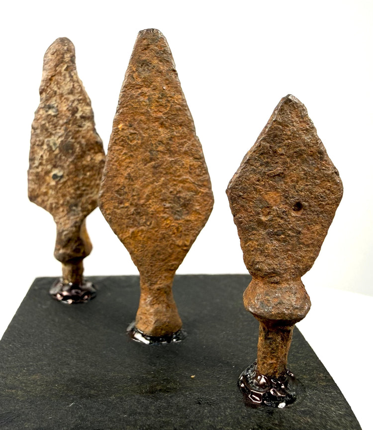 Elongated asymmetrical iron projectile point with a narrow blade, irregular edges, and reddish-brown oxidation.