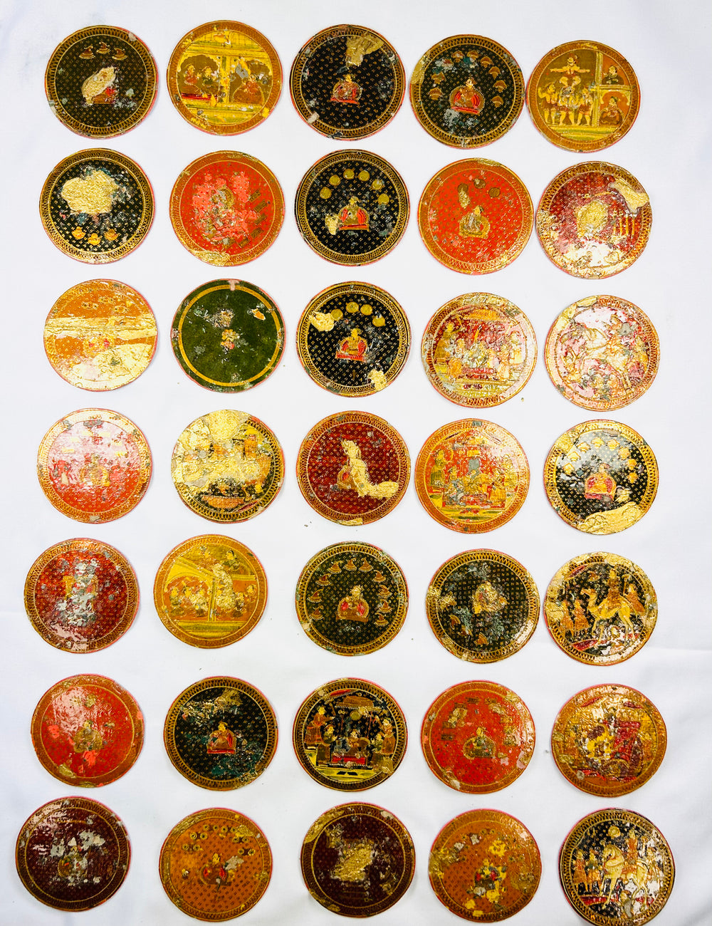 Group of antique Indian Ganjifa round playing cards featuring vibrant hand-painted mythological and courtly scenes, arranged neatly on a white backdrop.
