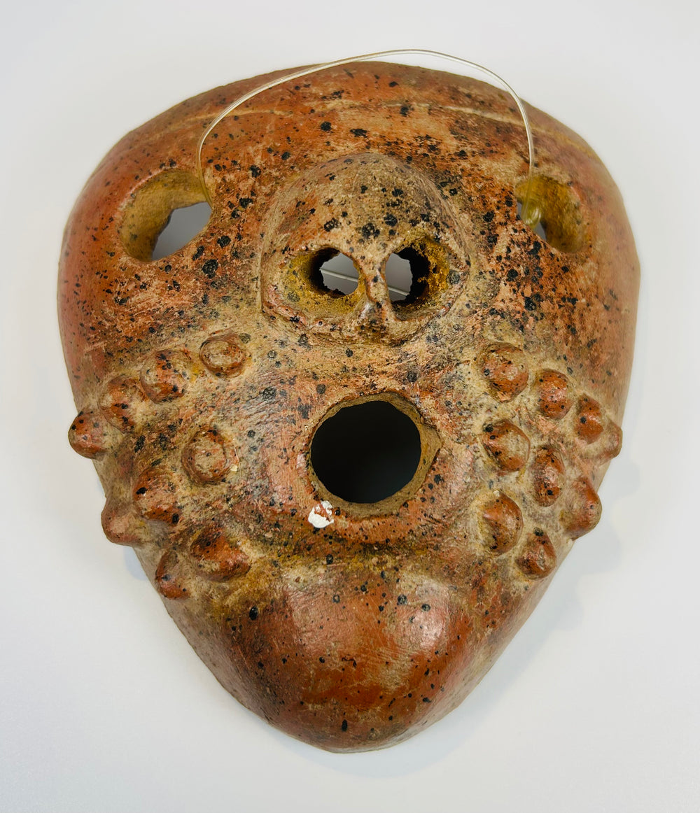 Pre-Columbian ceramic mask with stylized facial features and mineral deposits