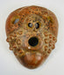 Pre-Columbian ceramic mask with stylized facial features and mineral deposits