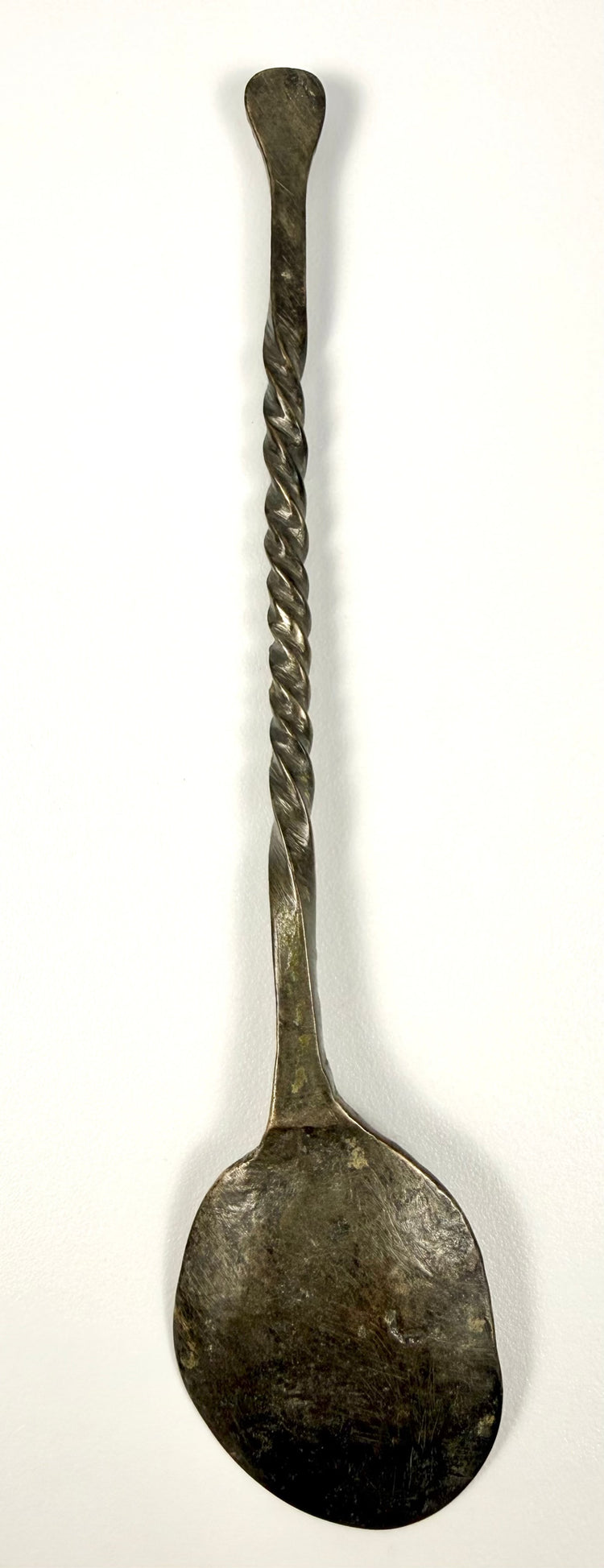 Side view of a 2nd-century Roman bronze spoon showing its slender twisted stem and gently rounded bowl.