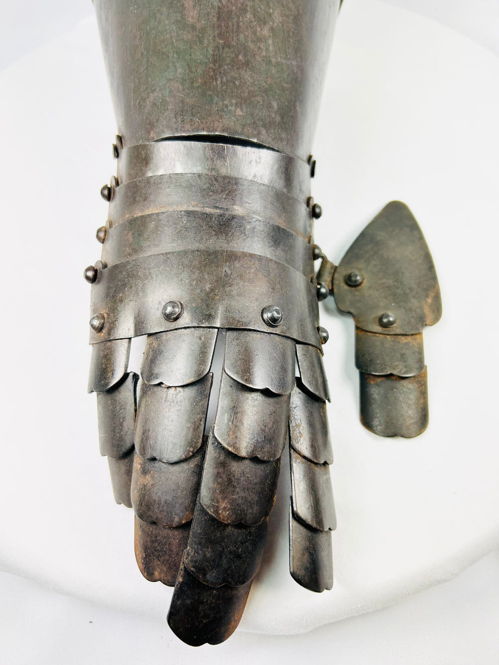 Historic European armour glove made of riveted steel, resting on white surface for detail clarity.