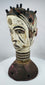 Nigerian ceremonial headdress featuring a dual-faced carved design, ringed neck, and perforated base.