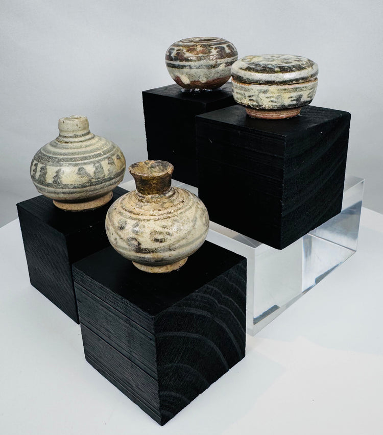 Four miniature Thai stoneware containers with transparent glaze and painted ornamentation, mounted on custom display stands.