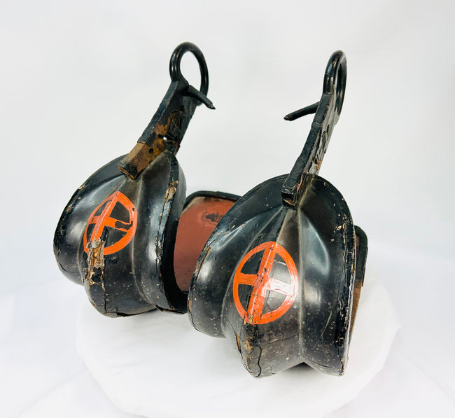 Close-up view of a pair of antique Japanese lacquered samurai stirrups from the Edo–Meiji period, featuring black lacquer with red cross-in-circle mon crests, displayed on a white background.