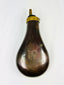 Antique 1840–1865 pressed copper powder flask with patriotic artillery and flag design, dark patina, brass collar and tapered spout, percussion firearm accessory.