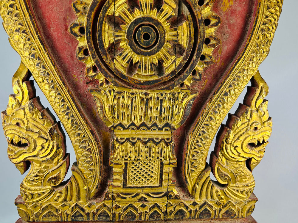 Late 19th century Thai carved teakwood shrine panel with gilded dharmachakra and twin naga serpents on red lacquer, architectural Buddhist ornament.