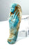 Ancient Egyptian funerary servant figurine featuring a slender mummiform body, raised arms across the chest, and weathered turquoise-blue faience.