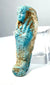Ancient Egyptian funerary servant figurine featuring a slender mummiform body, raised arms across the chest, and weathered turquoise-blue faience.