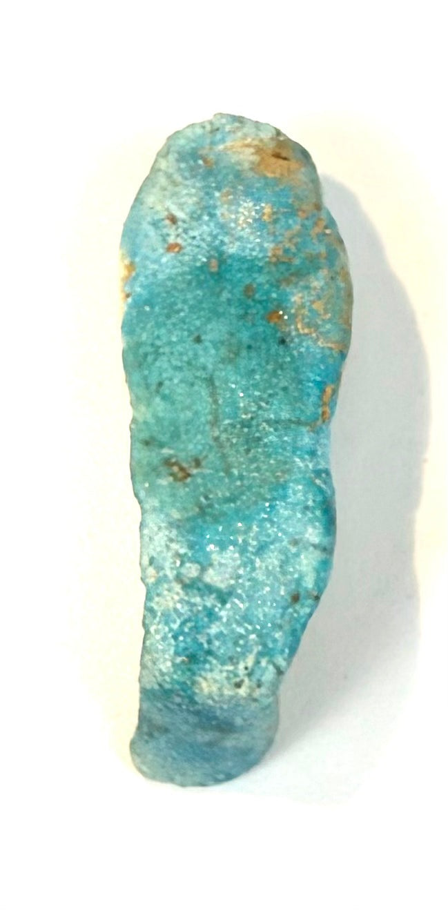 Ancient Egyptian miniature faience figure displaying raised arm detailing, a stylized wig, and scattered mineral-like deposits across its surface.