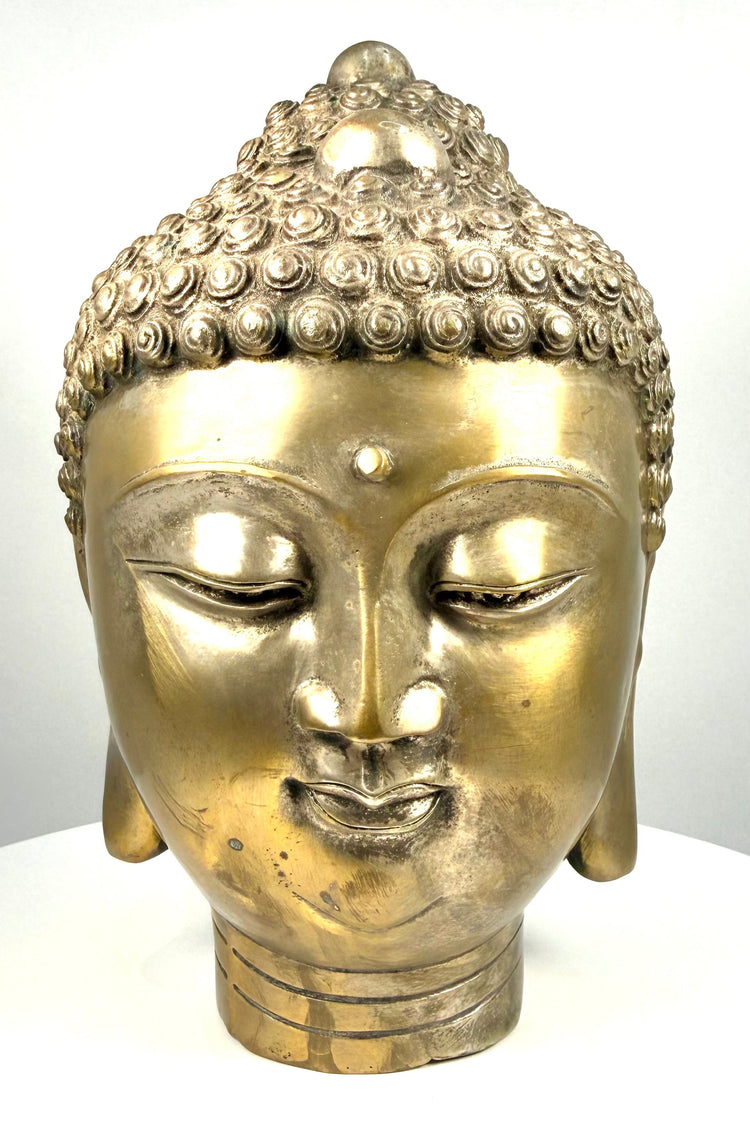 Golden metal Buddha head sculpture featuring a prominent urna on the forehead, rounded cheeks, and a peaceful meditative expression.