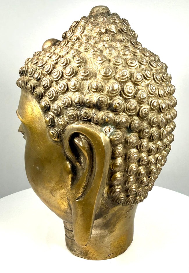 Antique-style cast-metal Buddha head featuring warm brass-like highlights, darker oxidation, and textured patination within the recessed sculptural details.