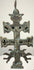 Spanish double-barred religious cross featuring sculpted religious figures, pierced openings, and a weathered surface with deep brown and green tones.