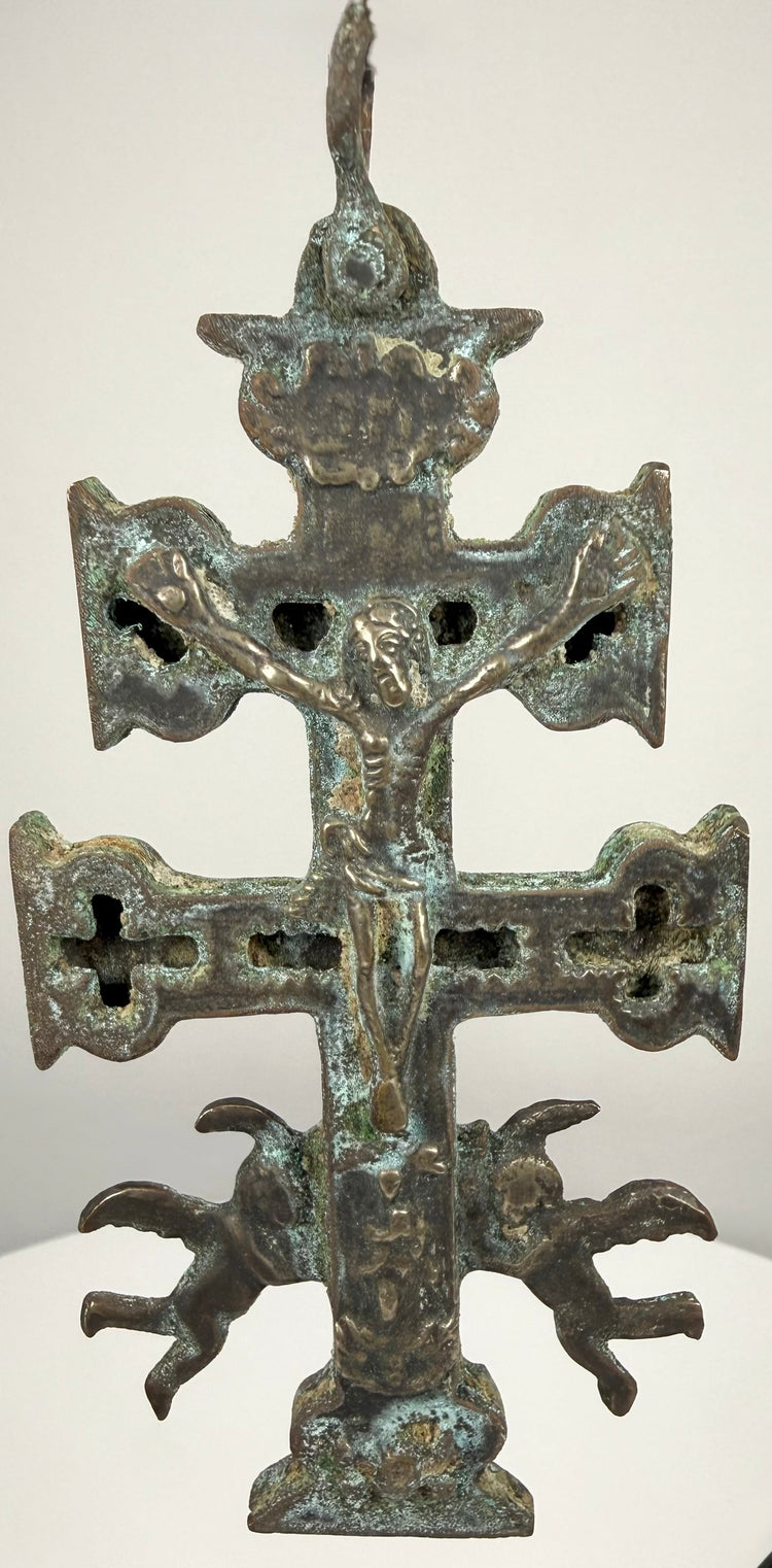 Spanish double-barred religious cross featuring sculpted religious figures, pierced openings, and a weathered surface with deep brown and green tones.