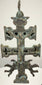 Spanish double-barred religious cross featuring sculpted religious figures, pierced openings, and a weathered surface with deep brown and green tones.