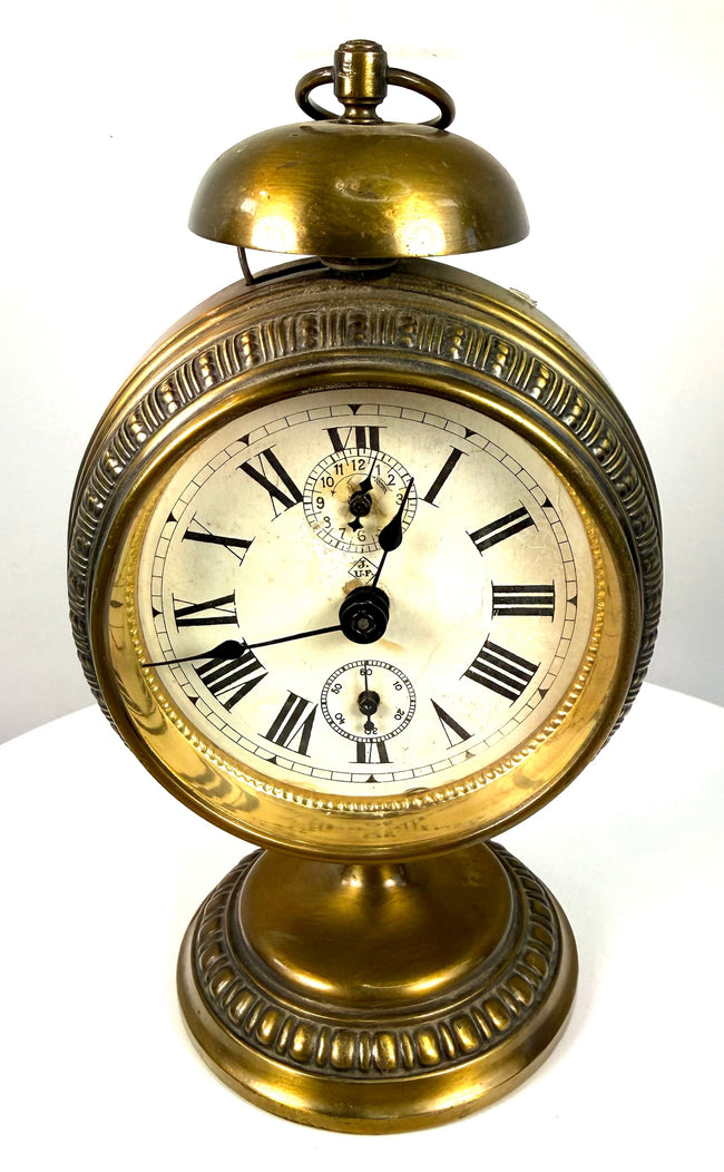 Early 20th-century Jahresuhrenfabrik alarm clock from Triberg, Germany, with decorative brass housing and an elevated pedestal base.
