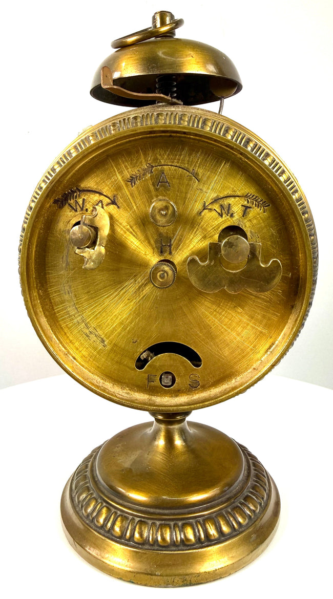 Early 1900s German mechanical clock featuring raised geometric brass decorations surrounding its circular case and pedestal base.