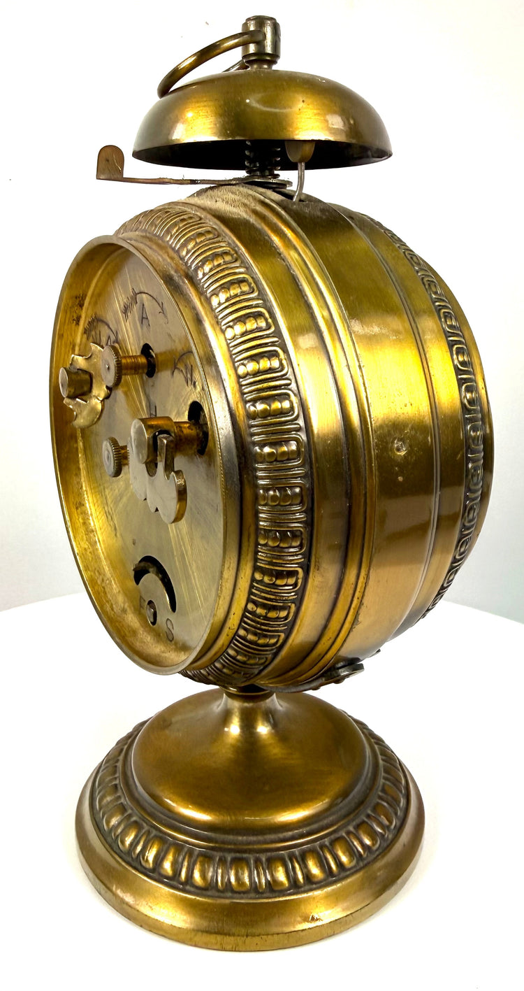 Antique German brass alarm clock with mechanical winding controls, engraved adjustment indicators, and traditional metal construction.