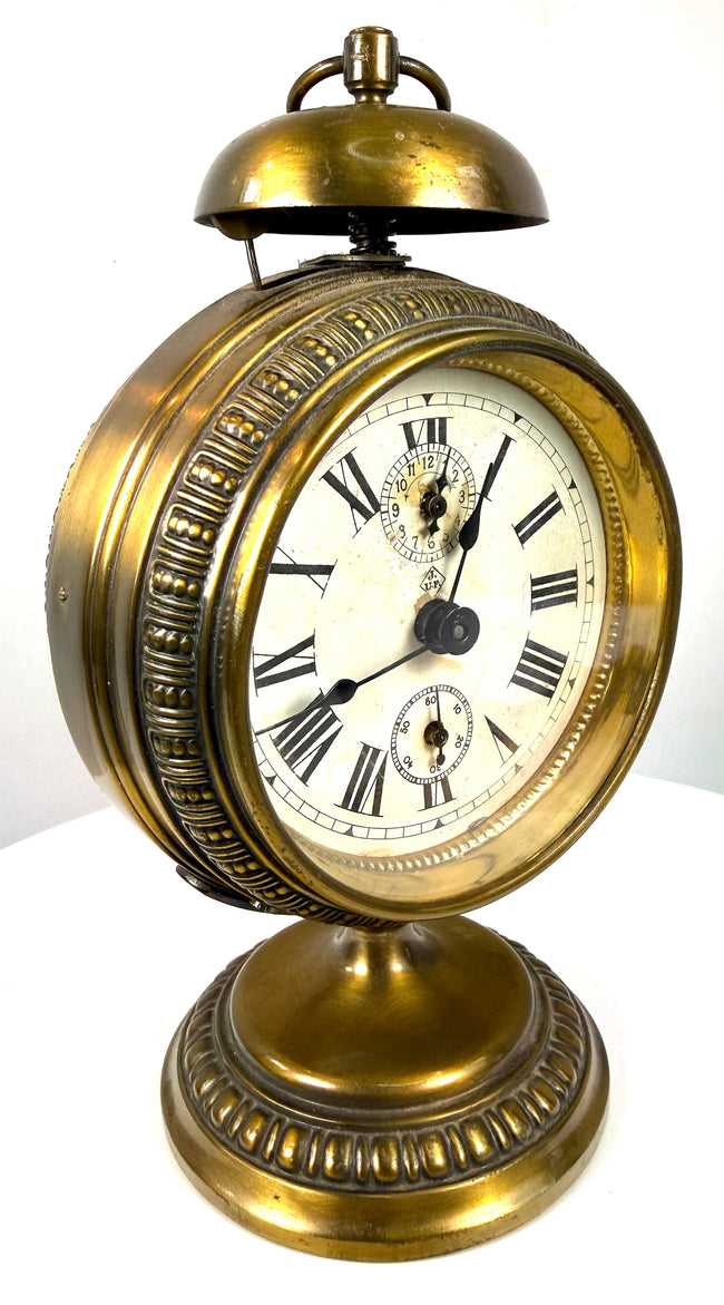 Decorative brass pedestal clock featuring a circular foot, raised ornamental detailing, and natural golden metallic patination.