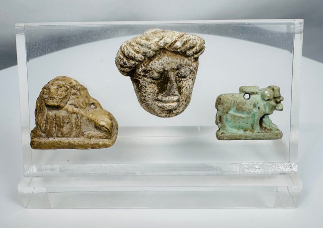 Ancient Egyptian and Greco-Roman antiquities mounted in a clear display case featuring religious and figural carvings.