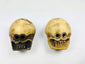 Front view of two Tibetan Citipati ritual beads carved from human femur bone, showing skull faces and suspension holes on a white background.