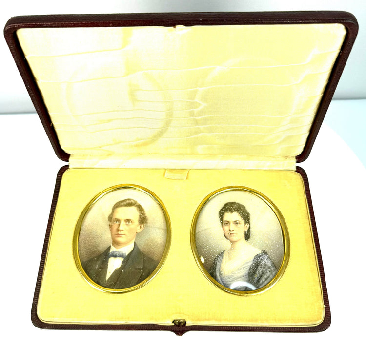 Open antique portrait presentation case featuring two oval colour portraits mounted in cream velvet beneath a patterned satin-like lid.