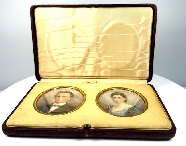 Angled view of a Victorian–Edwardian double portrait case showing the paired miniature likenesses and decorative cream-coloured interior.