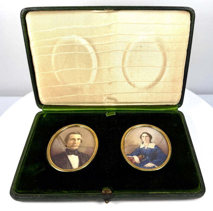 Open antique double portrait case featuring two oval colour miniatures, gilt-coloured metal surrounds, and cream patterned interior lining.