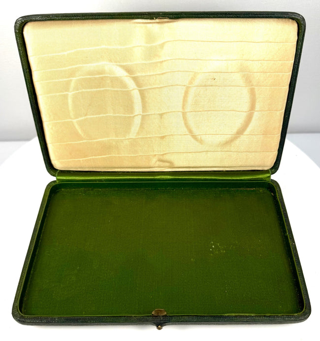 Angled view of an open Victorian–Edwardian presentation case showing paired oval portraits and decorative cream satin-like lining.