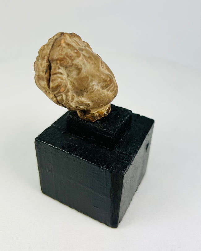 Classical-era head fragment with stylized facial features and warm patina, mounted on display base