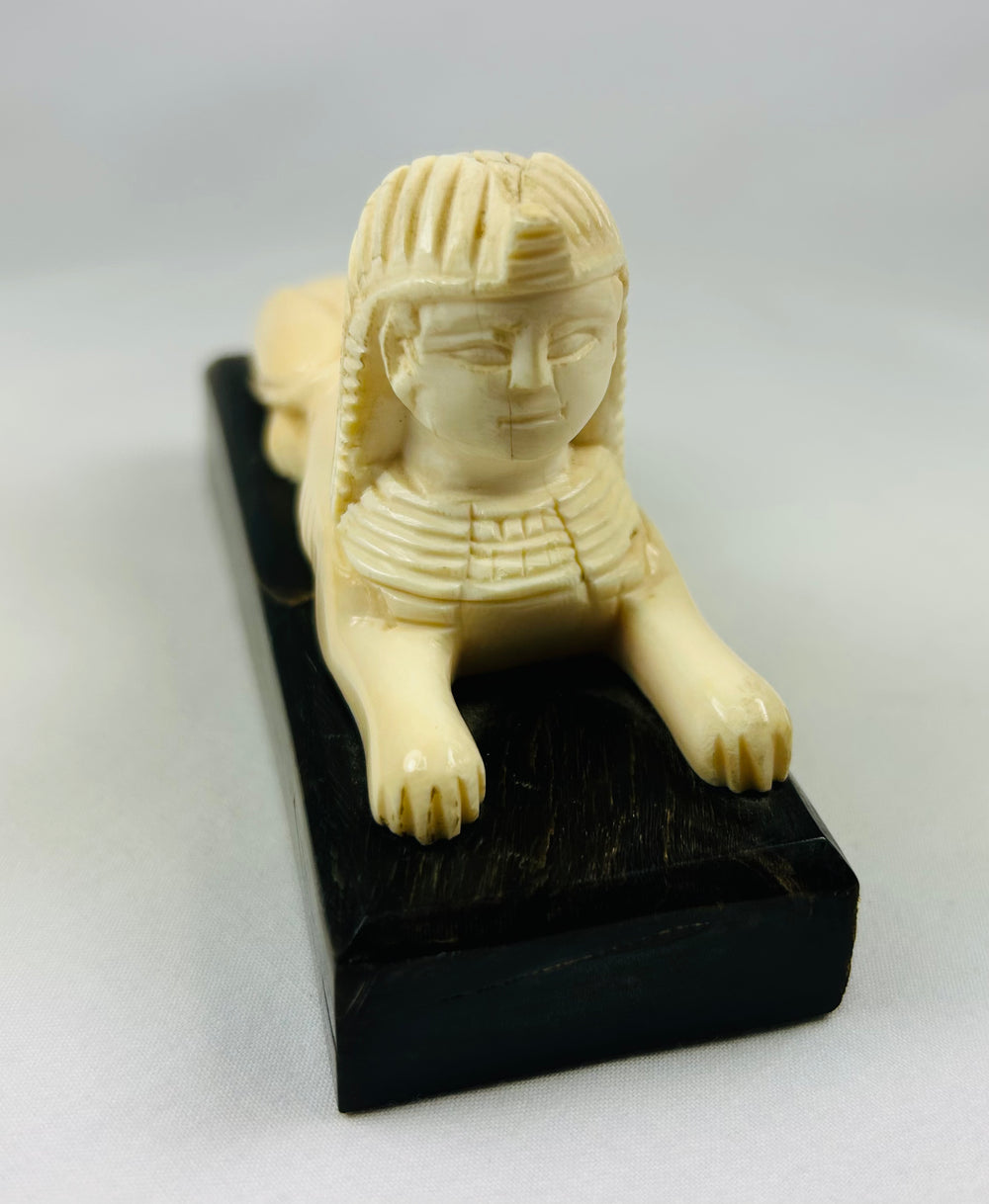 Decorative carved sphinx inspired by ancient Egypt, polished ivory-toned surface on stepped base