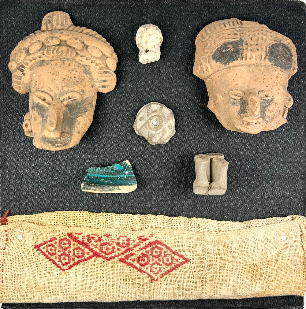 Pre-Columbian shadowbox with terracotta fragments, figurines, and red patterned textile on white background