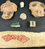 Pre-Columbian artifacts in black shadowbox, including figurines, mask shards, and geometric textile