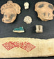 Pre-Columbian artifacts in black shadowbox, including figurines, mask shards, and geometric textile