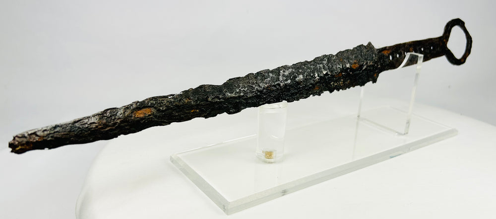 Medieval European dagger with ring pommel and corroded forged steel blade on acrylic display stand — 14th-century weapon artifact photographed on white background.